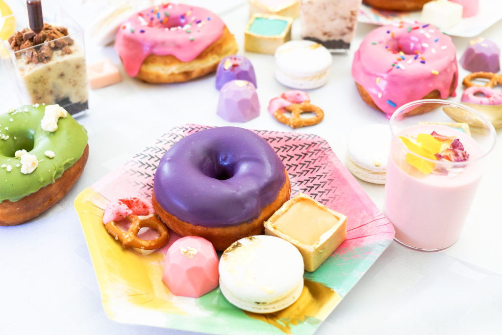 Donuts, mini chocolates, macarons and dessert cups on a plate