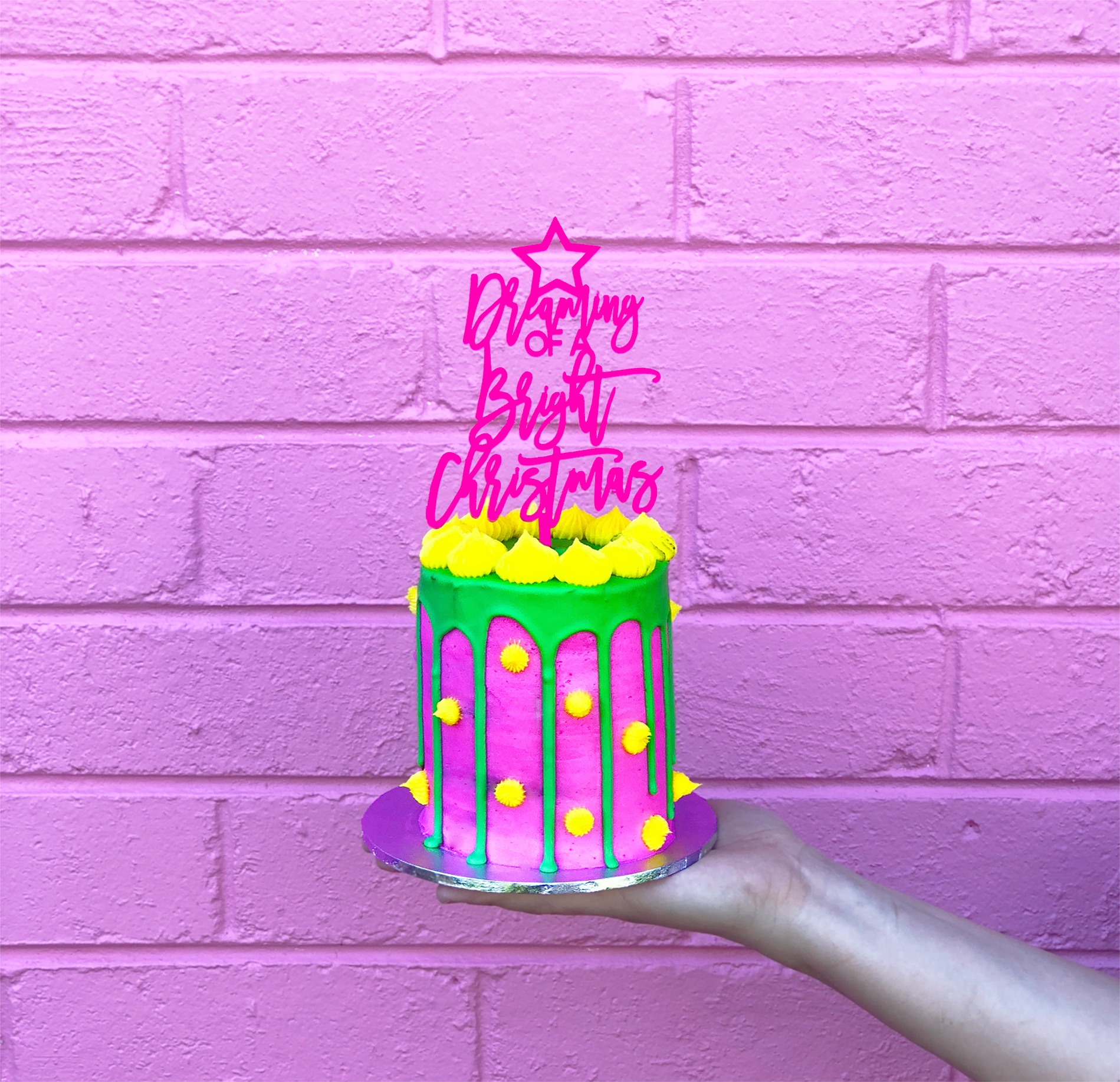 Mini neon cake and Christmas cake topper against a pink wall